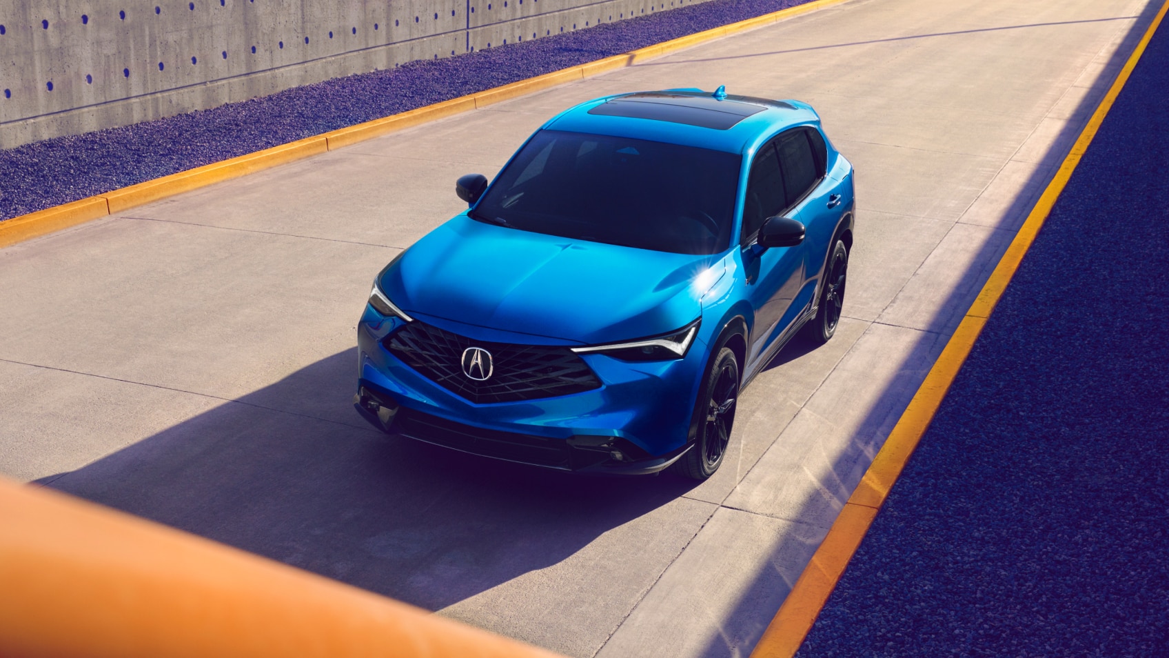 Plan grand angle en plongée d’un Acura ADX bleu sur une route.