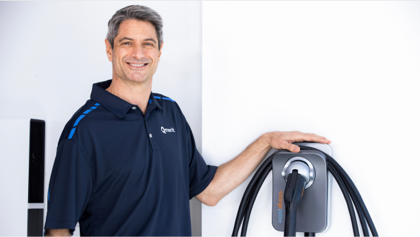 Un électricien portant un chandail de golf Qmerit debout à côté d’une borne de recharge murale ChargePoint+.