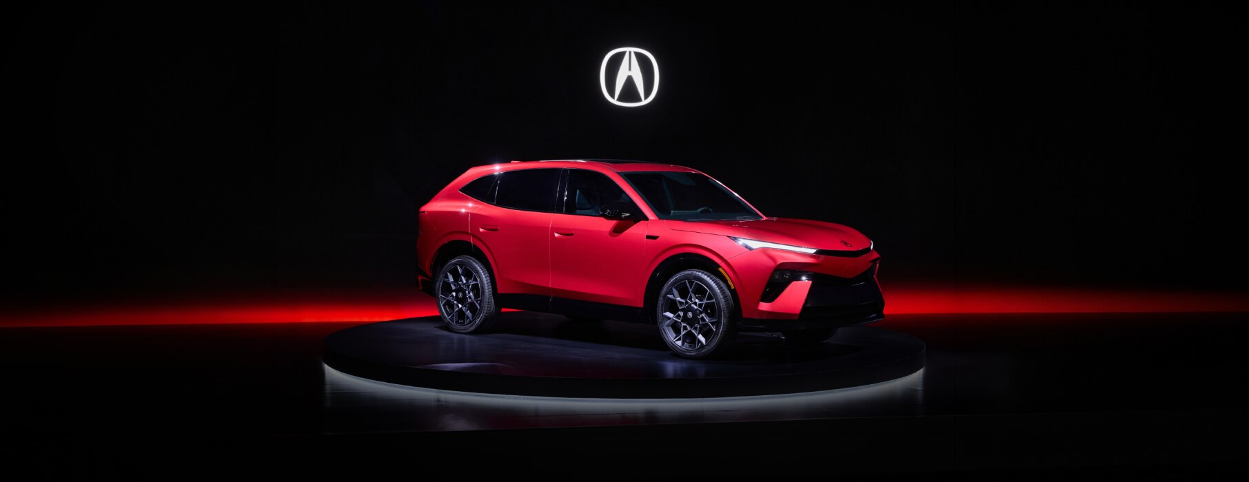 Acura Hybrid SUV Prototype shown on a on a dark studio stage with a glowing red light strip and Acura logo embedded  