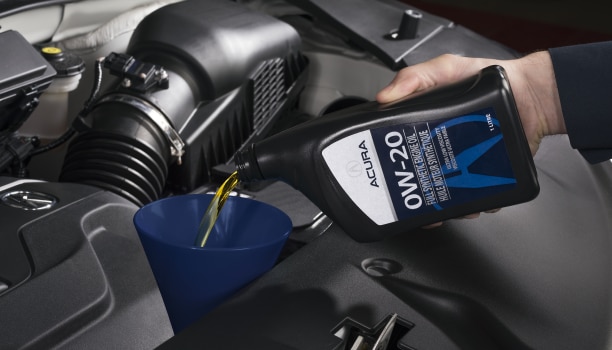 Closeup of an Acura Technician’s hand pouring engine oil into a funnel.
