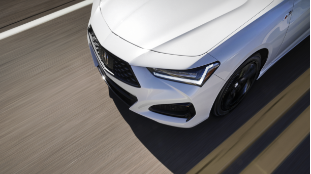 Partial view of a white Acura vehicle driving down a road.