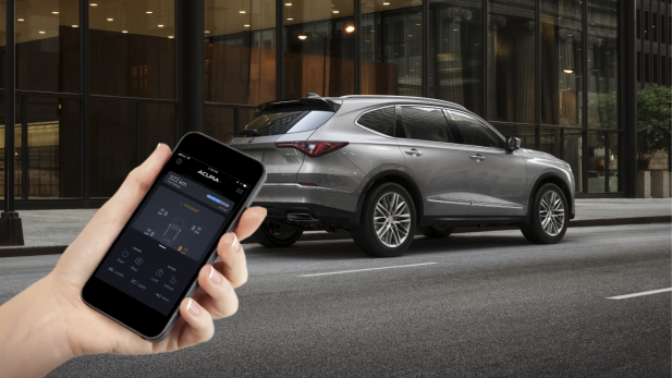 A person holds a phone in front of a parked Acura vehicle using the AcuraLink™ app. 