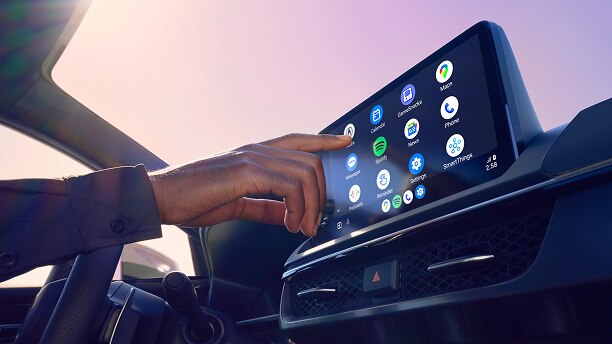 Gros plan d’une main utilisant la technologie Google intégrée sur l’écran du tableau de bord. 