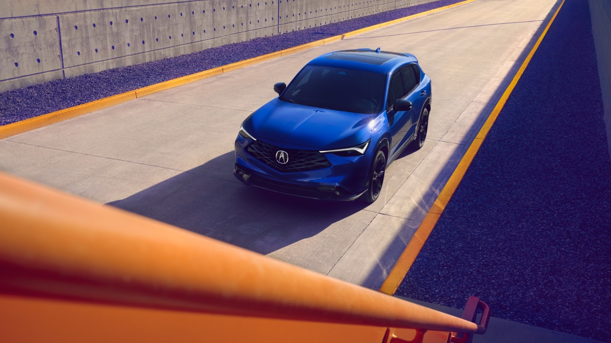 Plan grand angle en plongée d’un Acura ADX bleu sur une route.