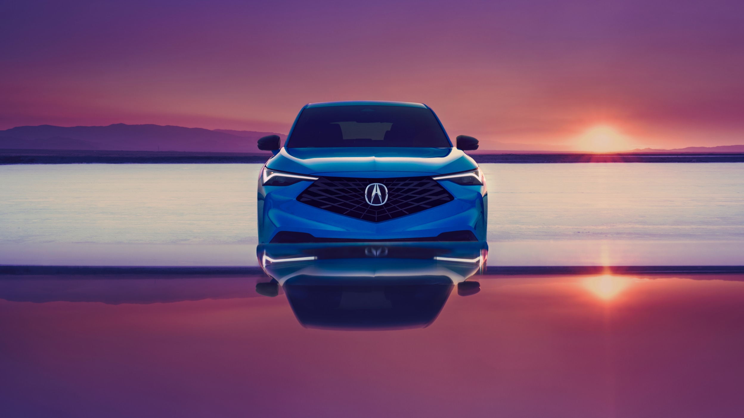Acura ADX bleu vu de face avec un coucher de soleil en arrière-plan.
