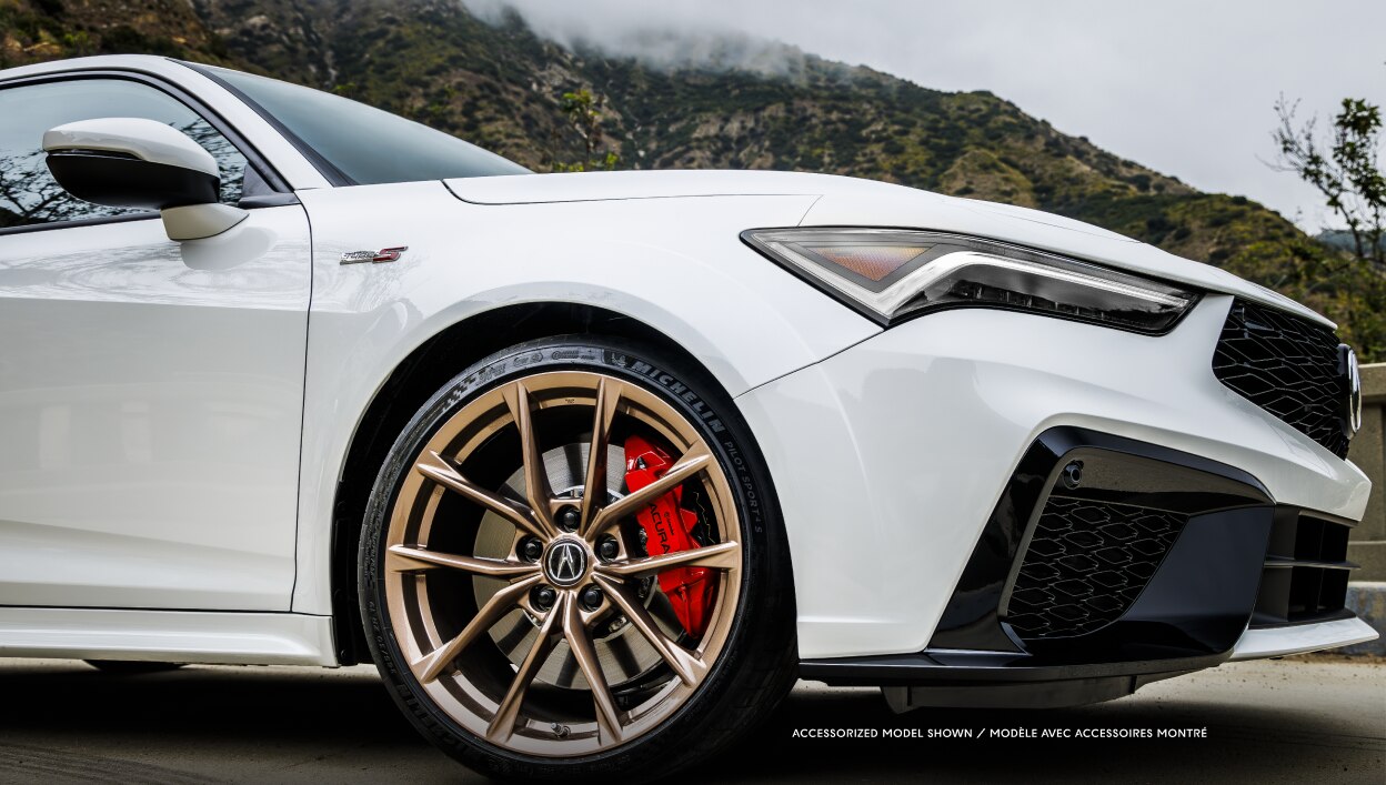 Side-view of a white Integra driving on an open road. 
