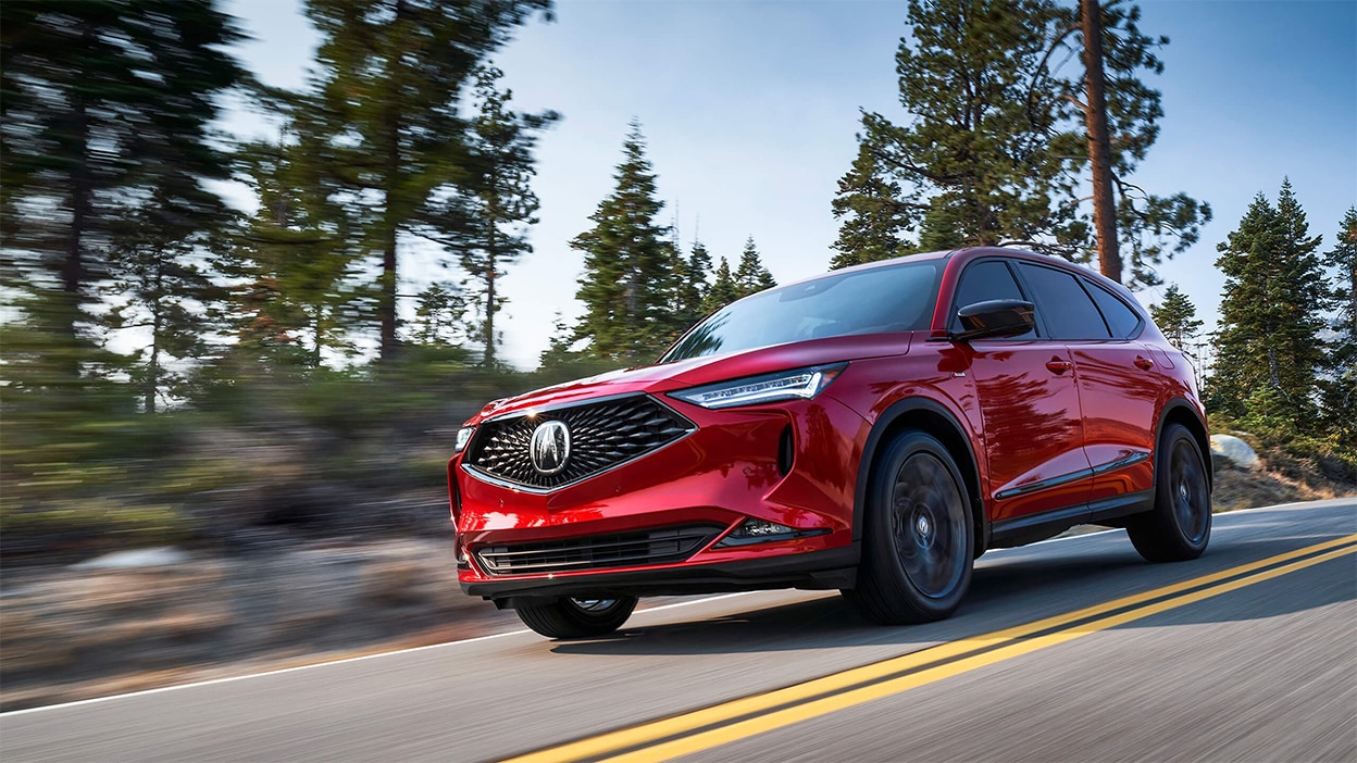 A red Acura MDX drives down a road in the wilderness.