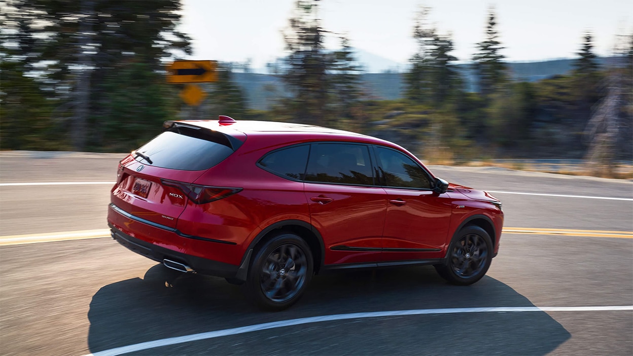 A red Acura MDX taking a corner in the wilderness.