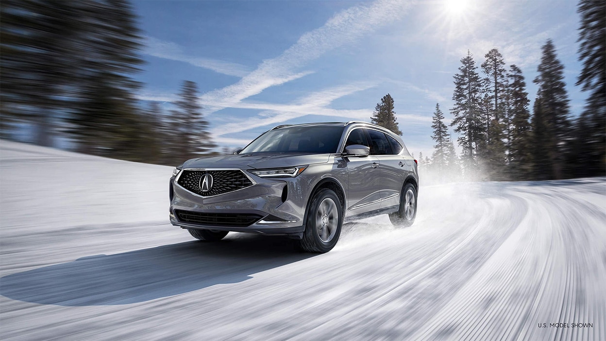 A grey Acura MDX driving down a snowy road in the wilderness.