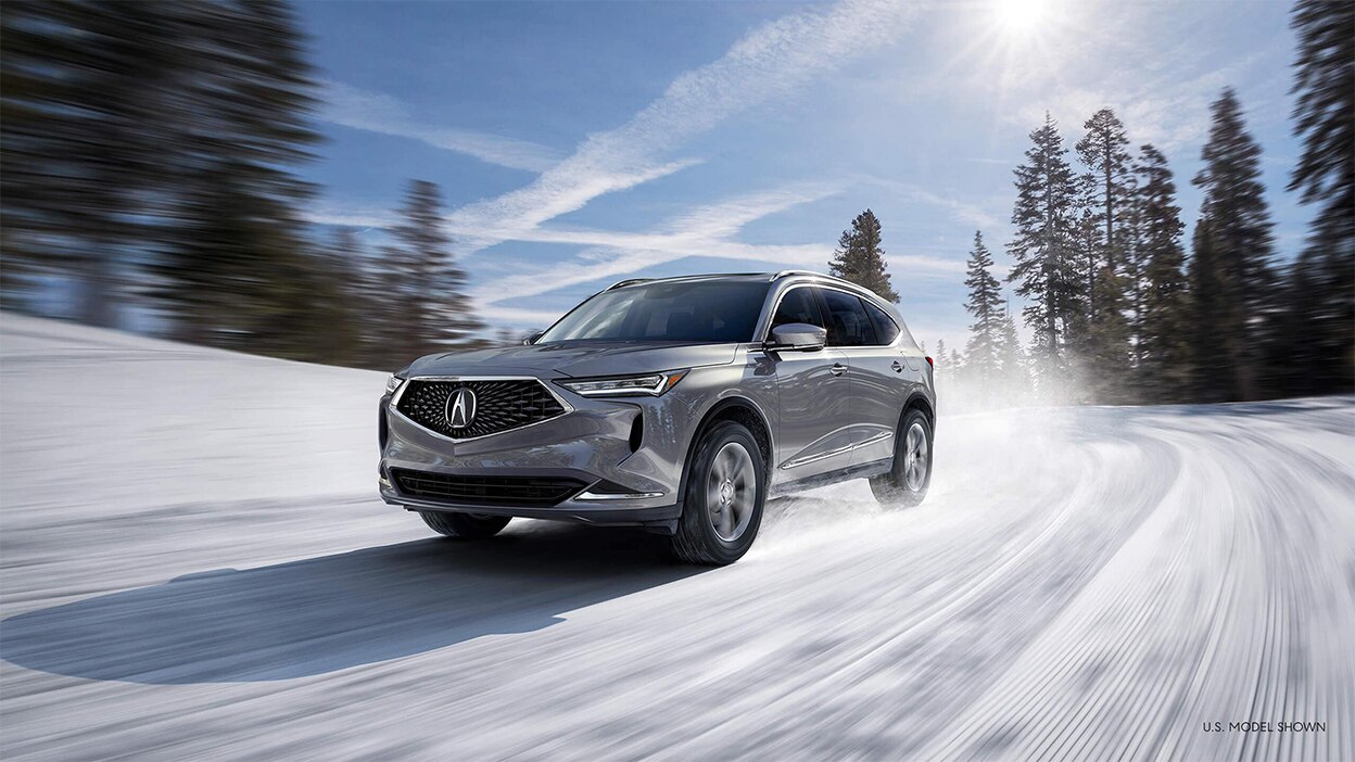 A grey MDX driving down a snowy road in the wilderness.