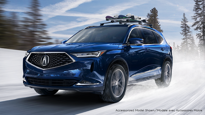 A blue Acura MDX with a snowboard rack driving down a snowy road. / Un MDX bleu avec fixation pour planche à neige circulant sur une route enneigée.