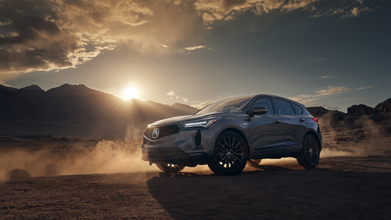 3/4 profile view of RDX in desert, with a low sun behind it. 