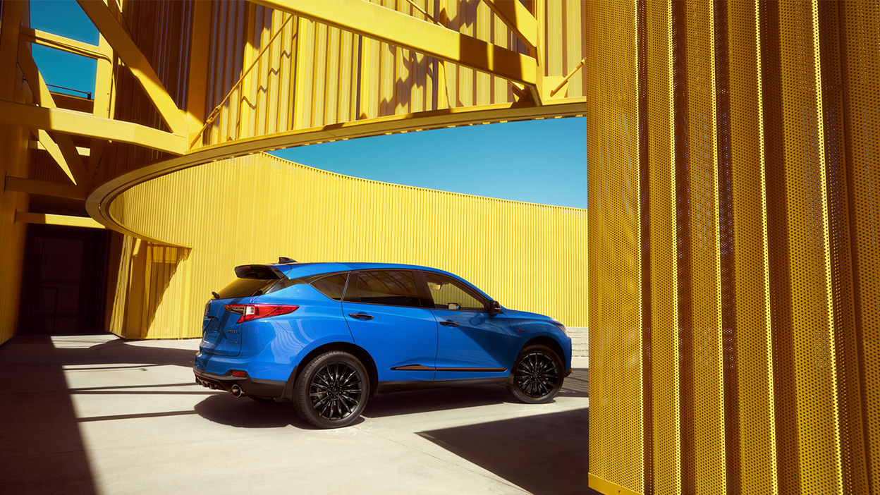 3/4 rear profile view of blue RDX outdoors amid a yellow walled structure. 