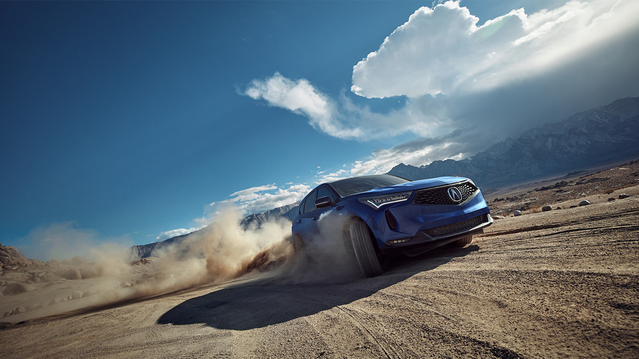 3/4 front view of blue Acura RDX driving on dirt road.