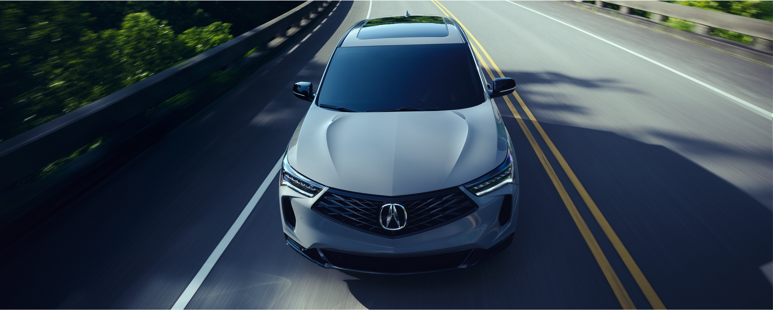 Vue 3/4 en plongée d’un RDX gris circulant sur l’autoroute par une journée ensoleillée.