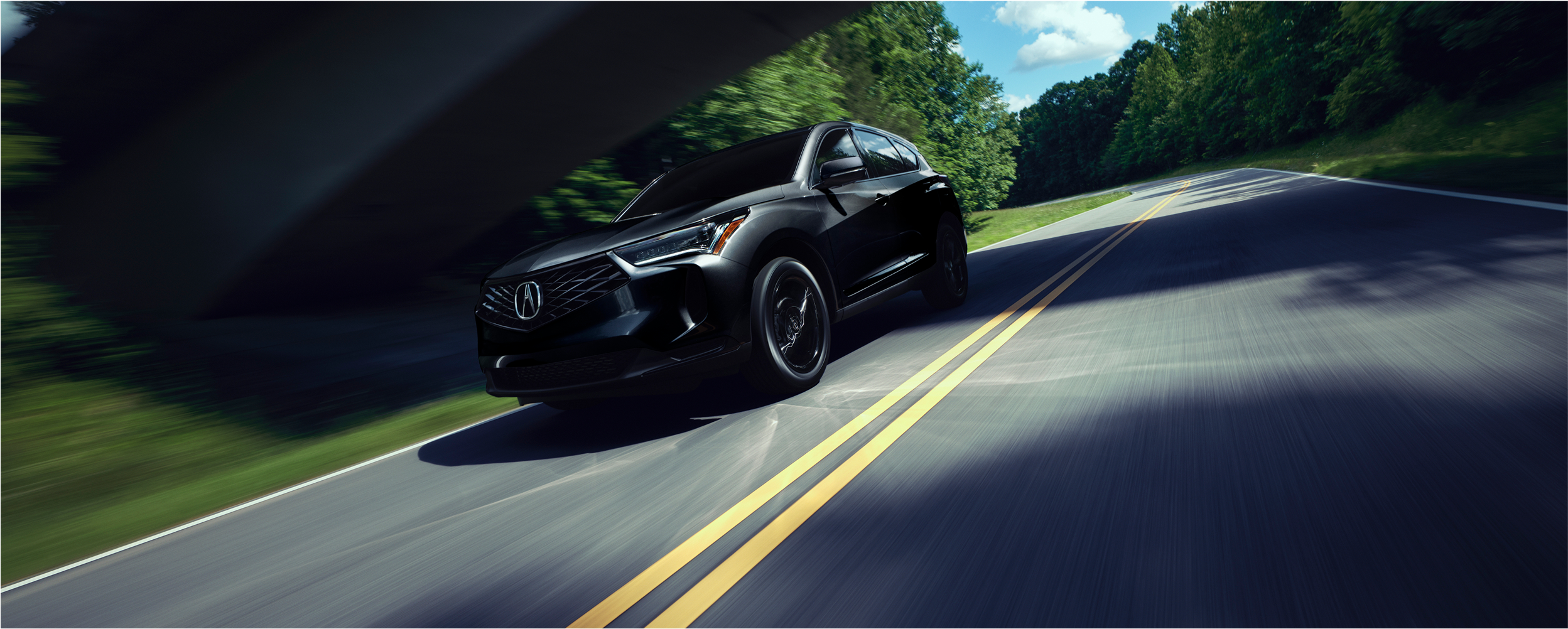 Vue 3/4 latérale d’un RDX noir circulant sur une autoroute de campagne pendant la journée.