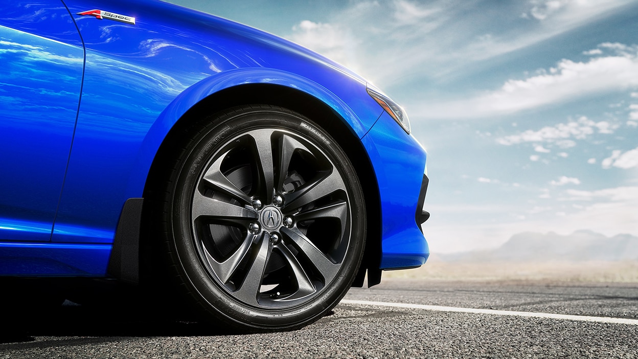 The front wheel of TLX in the foreground. Mountains, clouds and blue sky in the background.