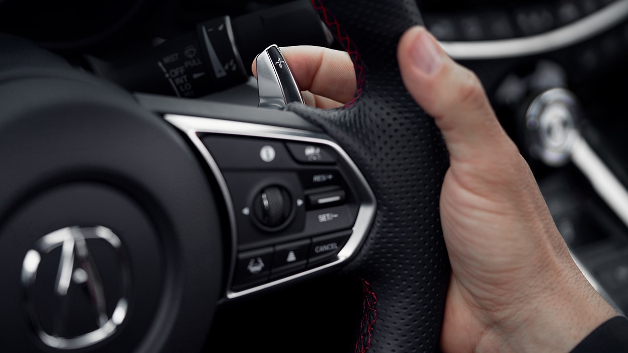 A hand pulls a paddle shifter behind the steering wheel.