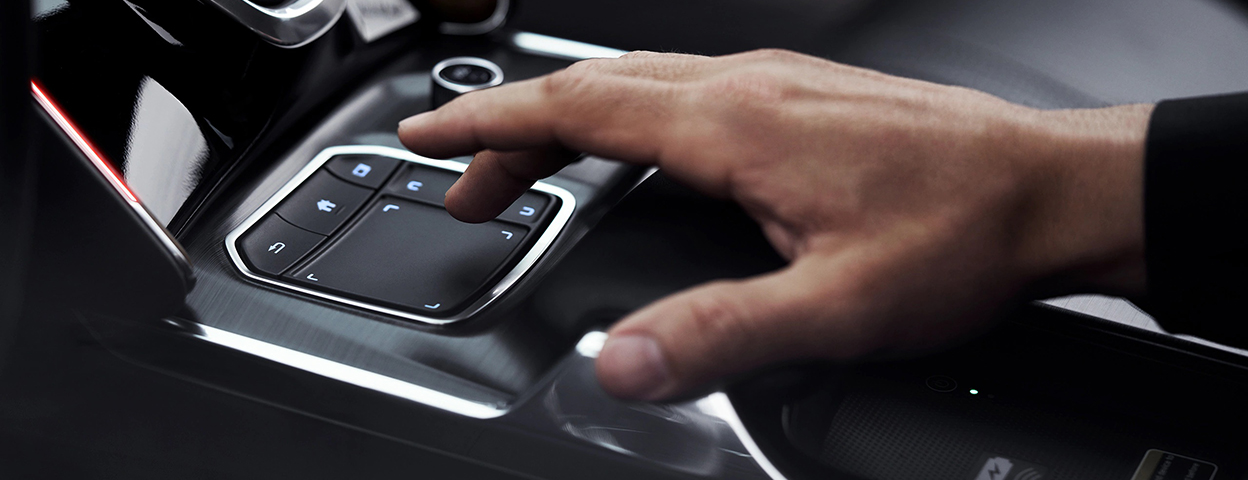 A hand hovers over the True Touchpad interface between the two front seats. / Une main survole l’interface True Touchpad entre les deux sièges avant.