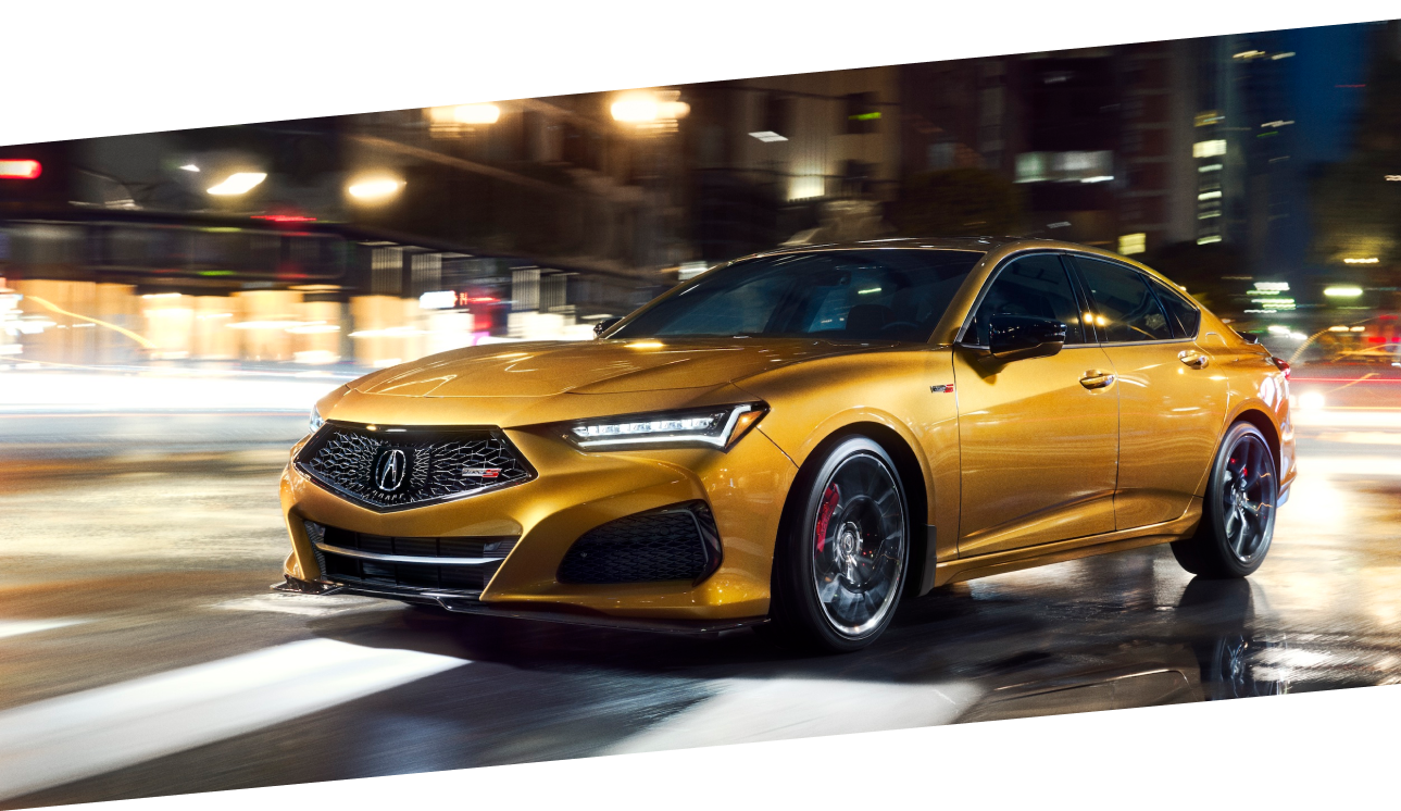 A gold TLX Type S driving on a city street at night. / TLX Type S de couleur or circulant sur une rue urbaine la nuit.