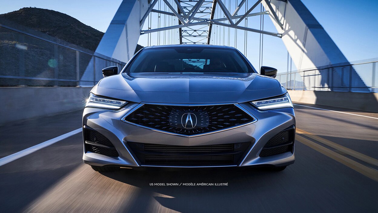 Front view of a grey Acura TLX driving over a bridge.