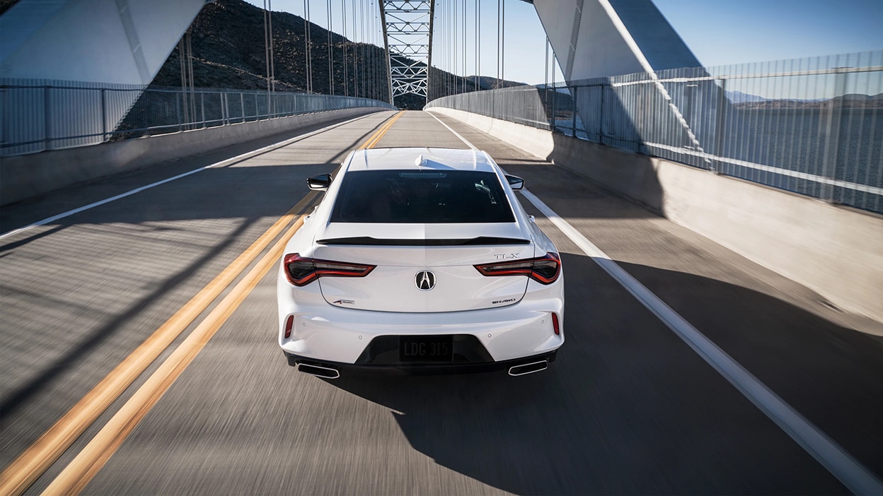 Rear view of a white TLX driving over a bridge.