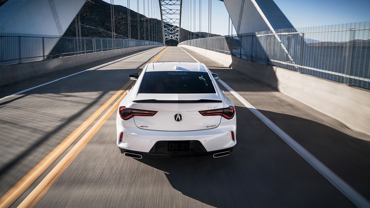 Rear view of a white Acura TLX driving over a bridge.