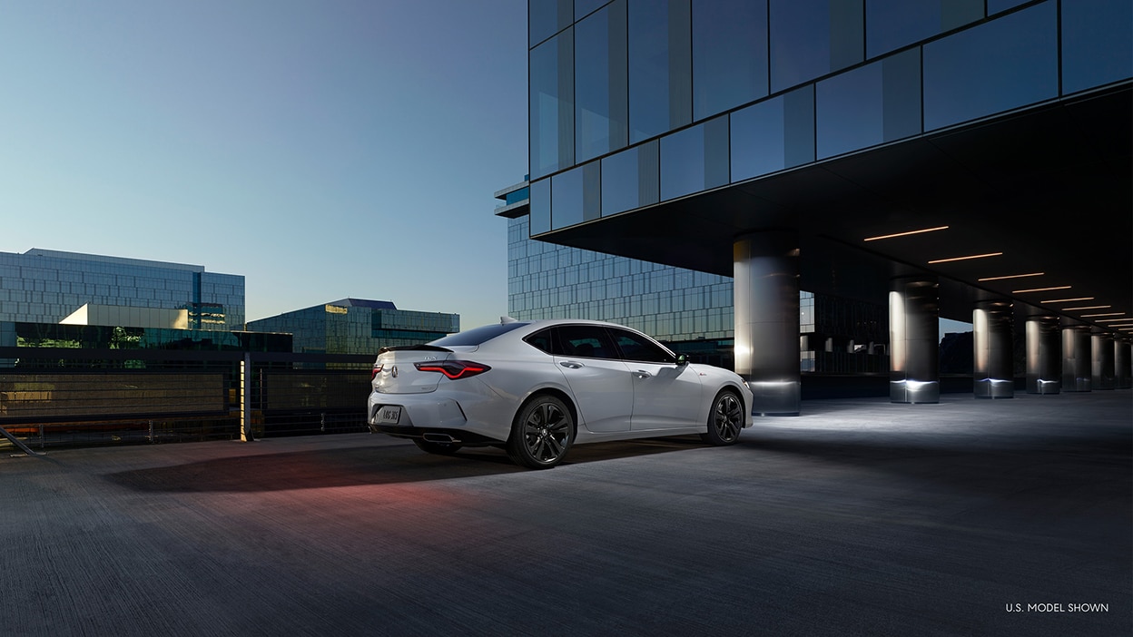 A white Acura TLX parked in front of an office building at night.