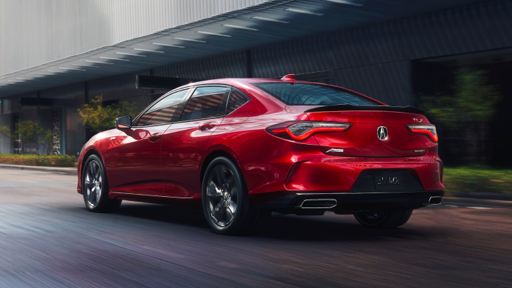 Rear view of a red Acura TLX A-SPEC driving past a building. / Vue arrière d’une TLX A-SPEC rouge qui passe devant un bâtiment.