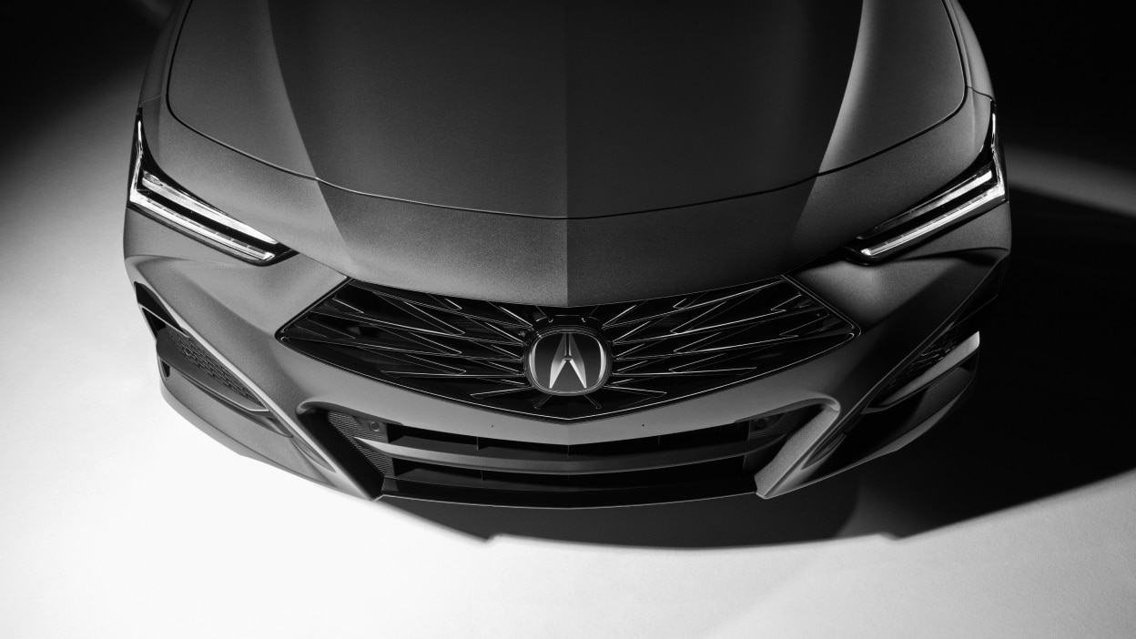 Rear view of a blue TLX and a white TLX driving beside each other towards a mountain range. 