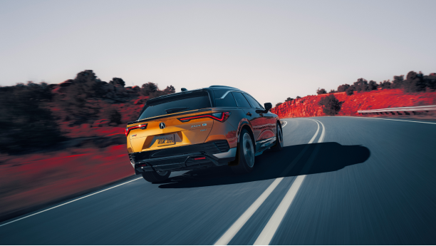 Plan de trois quarts arrière d’un ZDX or roulant sur une autoroute de montagne. Une partie de l’image est saturée de couleur, de sorte que la poussière sur les côtés de l’autoroute est rouge.