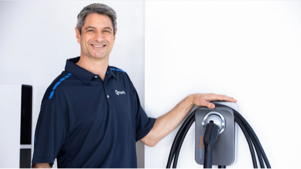 Electrician wearing a Qmerit golf shirt standing next to a wall-mounted ChargePoint+ charging unit.