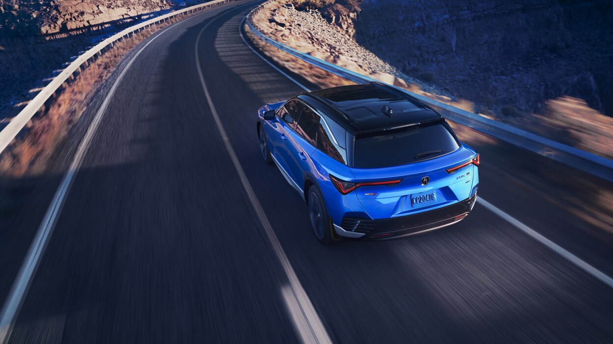 Plan de trois quarts arrière en plongée d’un ZDX bleu qui prend un virage sur une autoroute désertique.