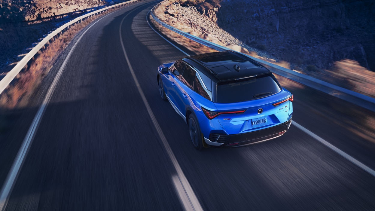 Plan de trois quarts arrière en plongée d’un ZDX bleu qui prend un virage sur une autoroute désertique.