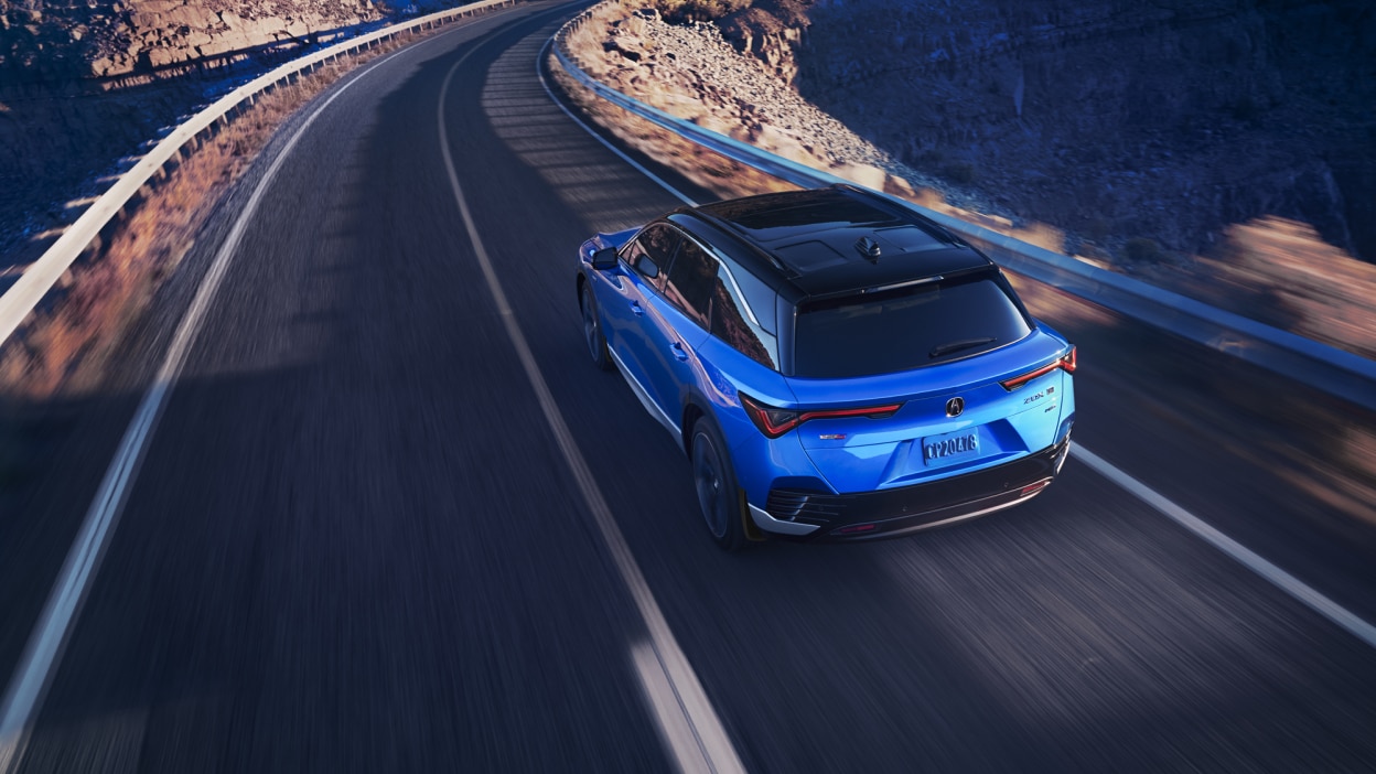 3/4 rear bird’s eye view of blue ZDX taking a turn on a desert highway.