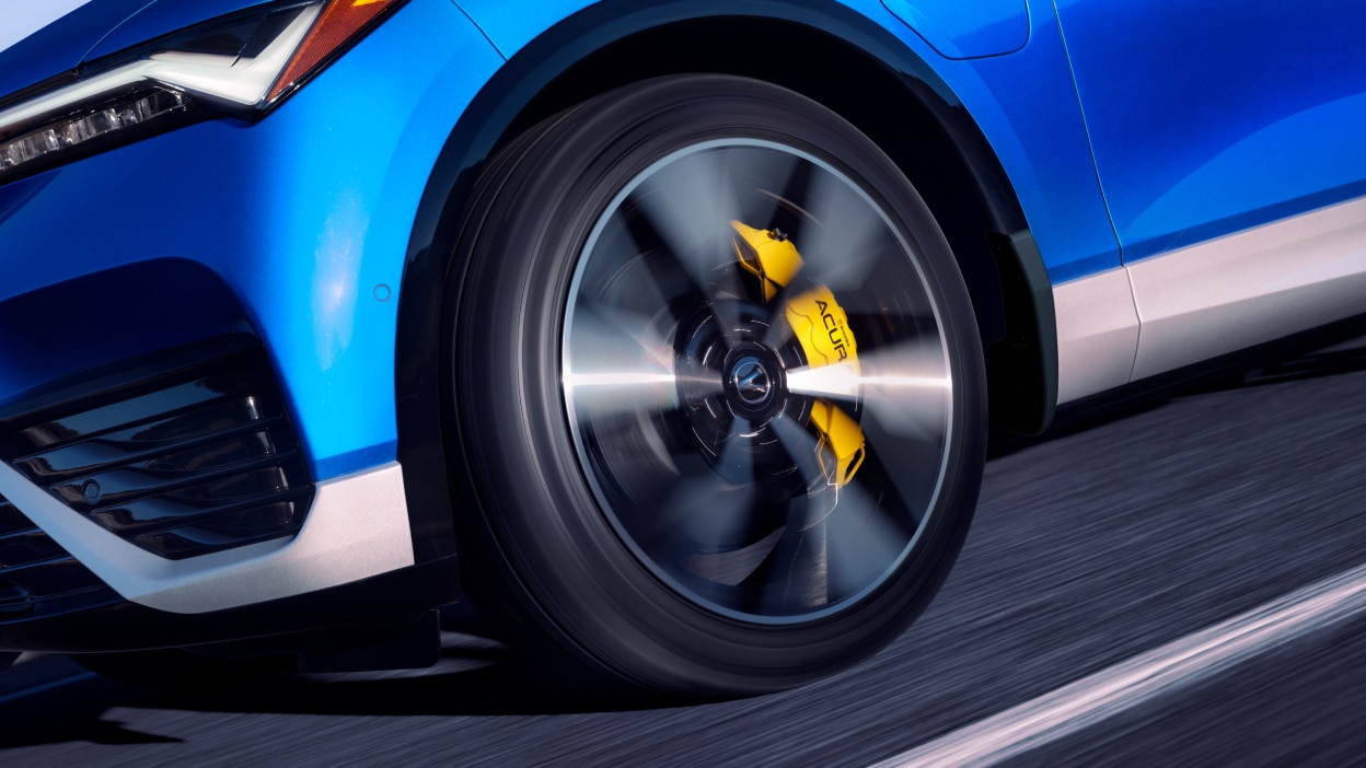 Closeup of wheel and yellow brake caliper on a blue ZDX that’s driving.