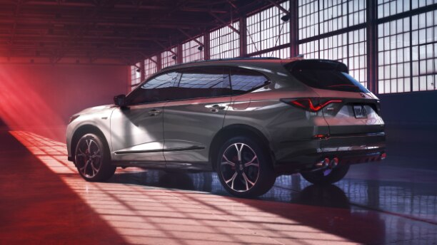 3/4 side rear view of grey MDX in an empty warehouse, lit partly with natural light and partly with red light.