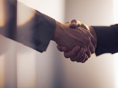 A close-up of two professionally dressed people shaking hands.  / Un gros plan de deux personnes en tenue professionnelle se serrant la main.