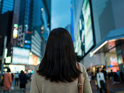 A woman walks down a busy city street.  / Une femme marchant dans une rue achalandée.