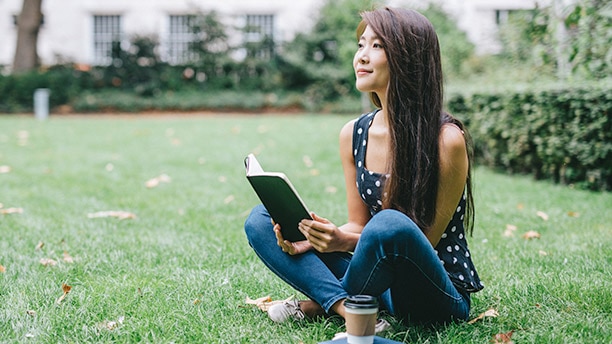 A young woman reading a book in a park./ Une jeune femme lisant un livre dans un parc