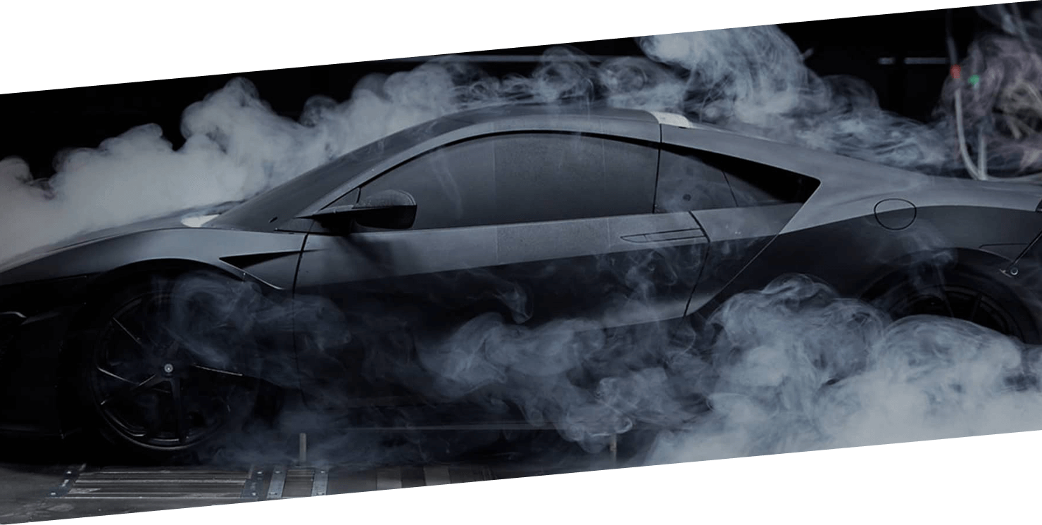 A Black Acura NSX spinning its rear wheels and producing smoke.	/ Une Acura NSX noire crée un nuage de fumée avec ses roues arrière.