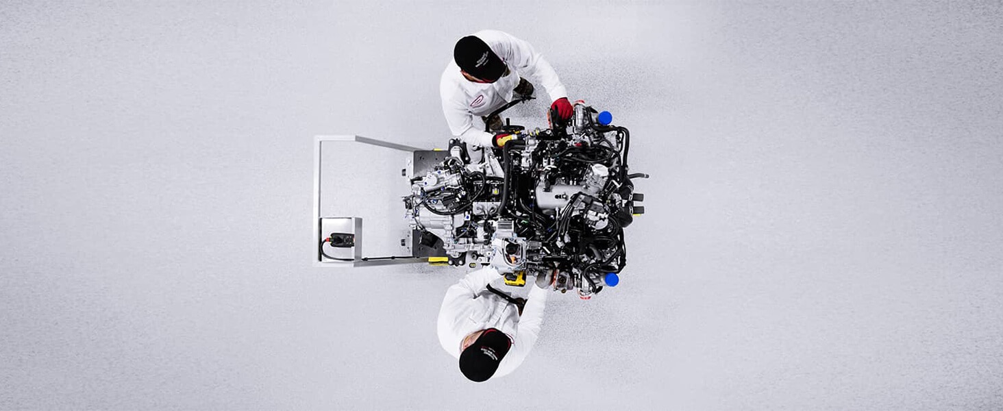 Overhead shot of two Acura engineers in whitespace, working on a futuristic engine.	Vue aérienne de deux ingénieurs Acura dans une salle blanche qui travaillent sur un moteur futuriste.
