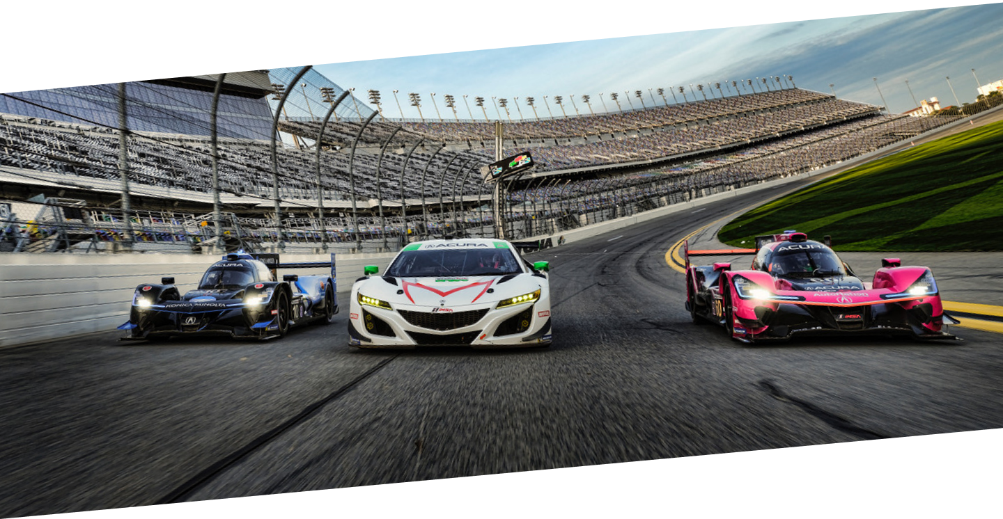 Front shot of a white Acura NSX GT3 flanked by a blue and a white Acura ARX on either side. The three cars are racing around a speedway with the stadium seating seen in the background.	Vue avant d’une Acura NSX GT3 blanche entre une Acura ARX bleue et une Acura ARX rouge. Les trois voitures participent à une course sur un circuit ovale avec les estrades en arrière-plan.