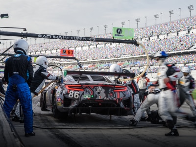 Rear view shot of an Acura NSX GT3 with custom red, white and grey sponsorship graphic wrap. A crew is seen working quickly around the car during a race pit stop.	Vue arrière d’une Acura NSX GT3 avec un habillage personnalisé rouge, blanc et gris. Une équipe de ravitaillement travaille rapidement autour de la voiture pendant un arrêt aux puits.