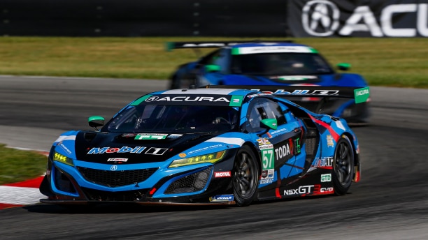 Head-on view of two blue Acura race cars speeding around the bend of a track, one in front of the other. 	Vue avant de deux voitures de course Acura bleues l’une derrière l’autre qui négocient une courbe sur un circuit de course.