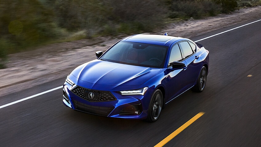 A blue Acura TLX drives down a highway in the desert. / Une Acura TLX bleue roulant sur une autoroute dans le désert.