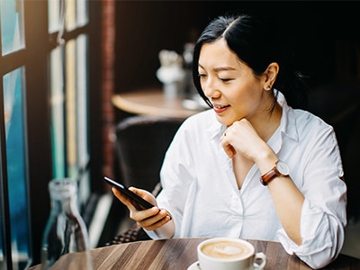 A young woman sits in a café and looks at a smart phone. / Une jeune femme est assise dans un café et regarde un téléphone intelligent.