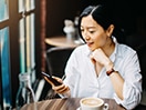 A young woman sits in a café and looks at a smart phone.  / Une jeune femme est assise dans un café et regarde un téléphone intelligent.