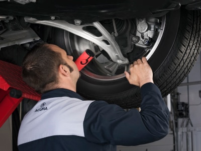A certified Acura mechanic is inspecting the tire from under the vehicle. // Un mécanicien Acura certifié inspecte le pneu sous le véhicule