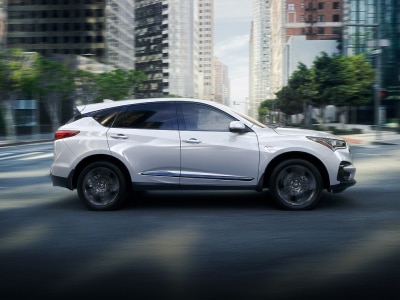 Side profile view of white Acura RDX while driving during the day through city. // Vue de profil latérale de l'Acura RDX blanc en conduisant pendant la journée à travers la ville